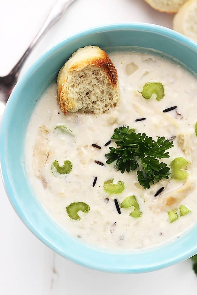 close up top view of chicken & wild rice soup with a slice of bread in a bowl with a spoon and mores slices of brew on the sid.