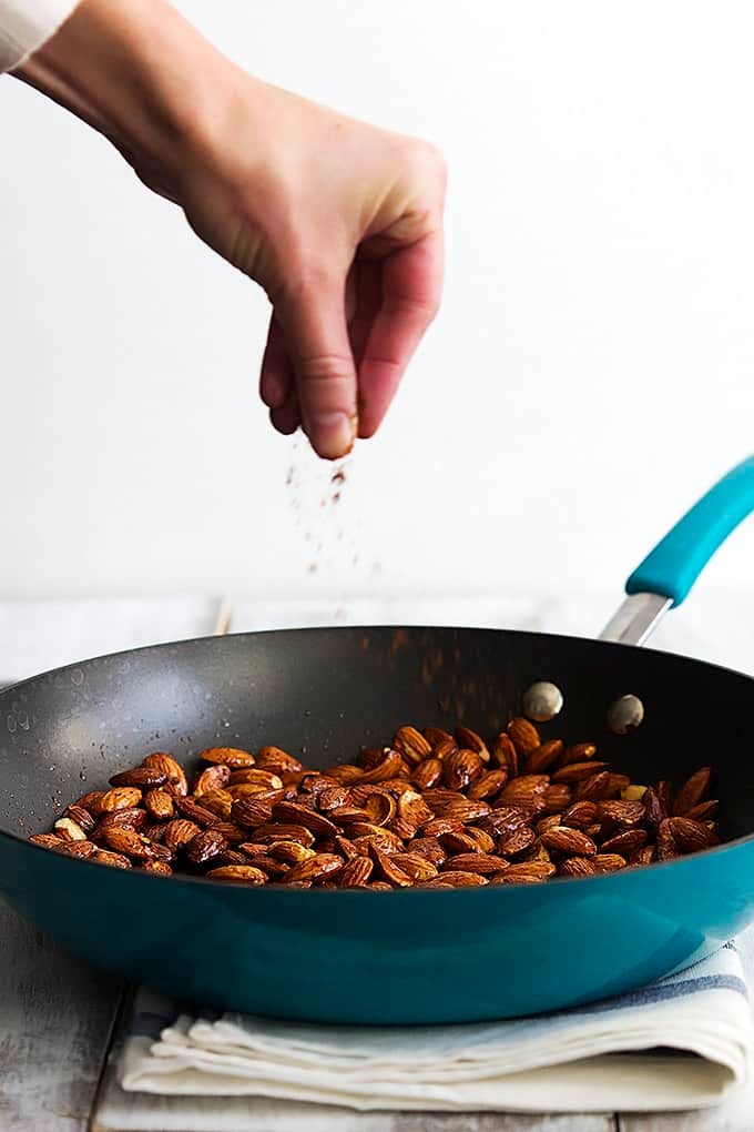a hand sprinkling spices over chili lime almonds in a skillet.
