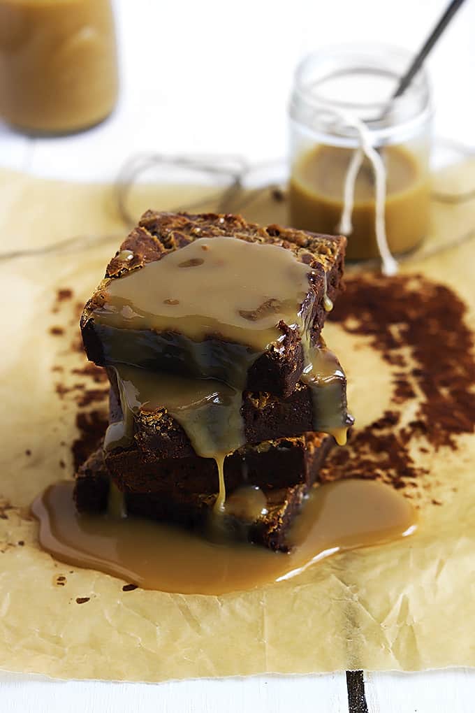 stacked Dulce de Leche brownies covered in Dulce de Leche sauce with more sauce in jars in the background.