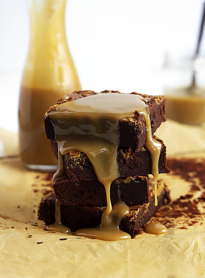 stacked Dulce de Leche brownies covered in Dulce de Leche sauce with jars of more sauce in the background.