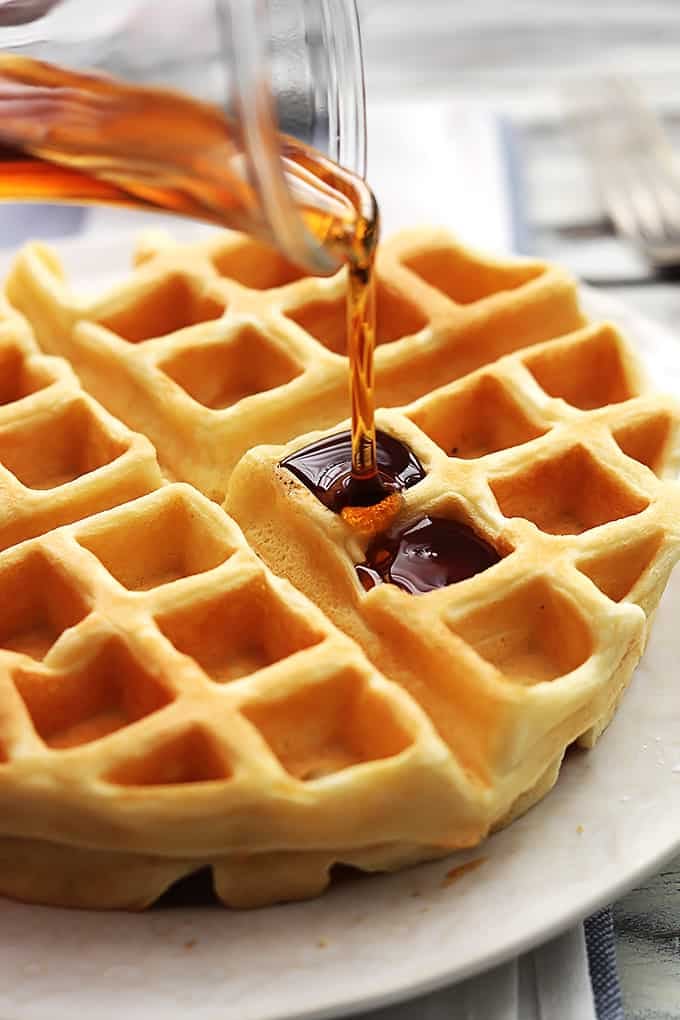 a Dutch cream waffle on a plate with syrup being poured on top.
