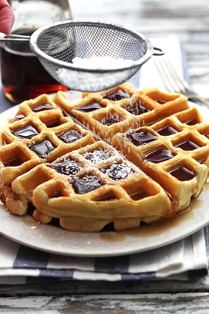 a sifter sifting powdered sugar on top of a Dutch cream waffle on a plate.
