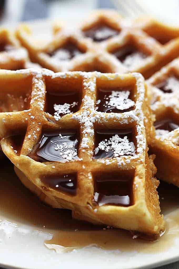 close up of a Dutch cream waffle topped with syrup and powdered sugar on a plate.