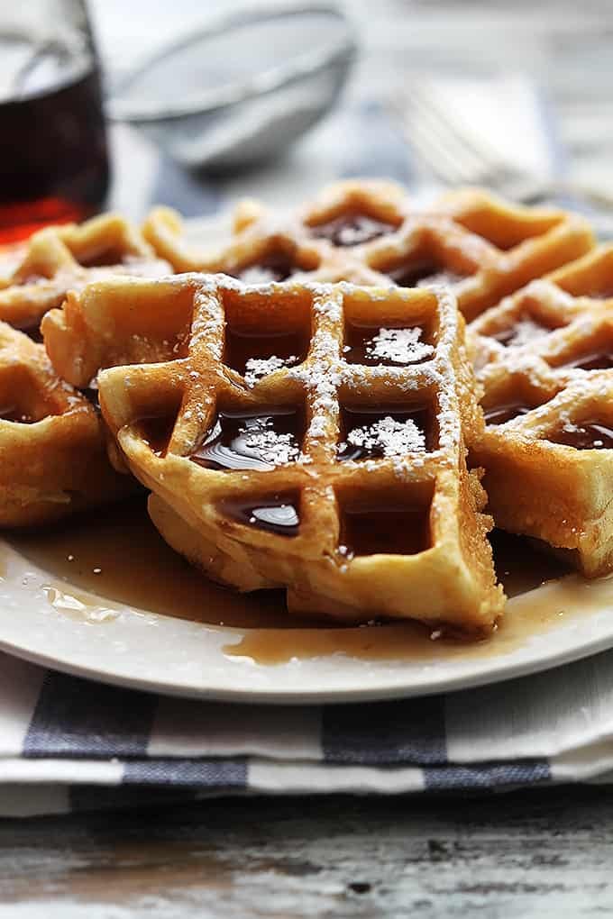 a Dutch cream waffle on a plate topped with syrup and powdered sugar.