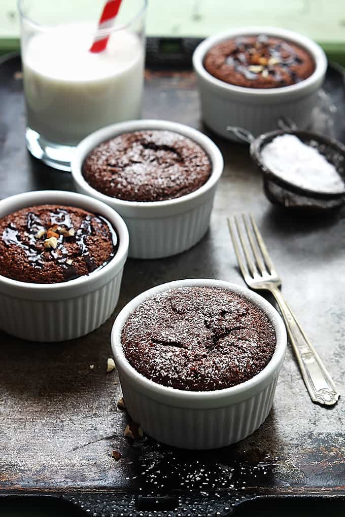 flourless chocolate almond cakes in small individual bowls with a fork, a sifter of powdered sugar and a glass of milk on the side.