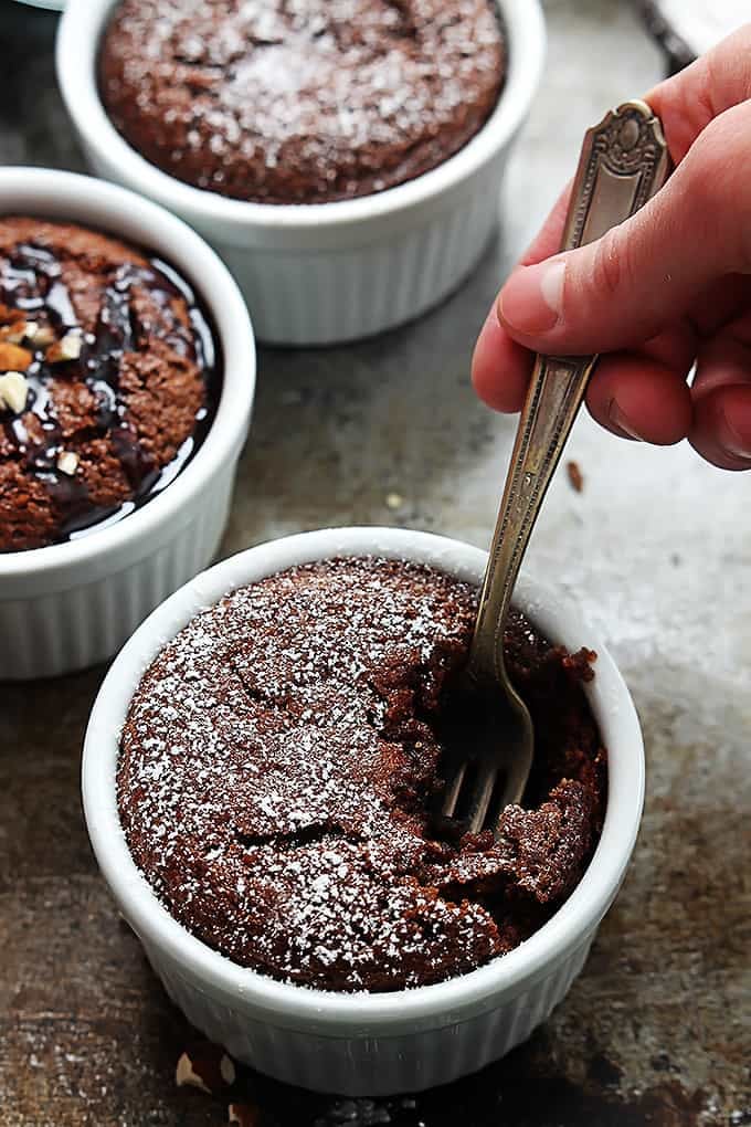 a hand holding a fork in a bowl of flourless chocolate almond cake with more bowls of cake in the background.