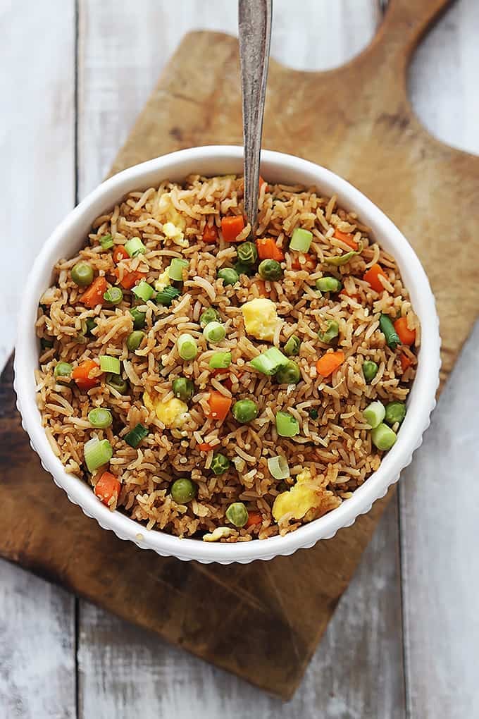 top view of a bowl of fried rice with a spoon on a wooden cutting board.