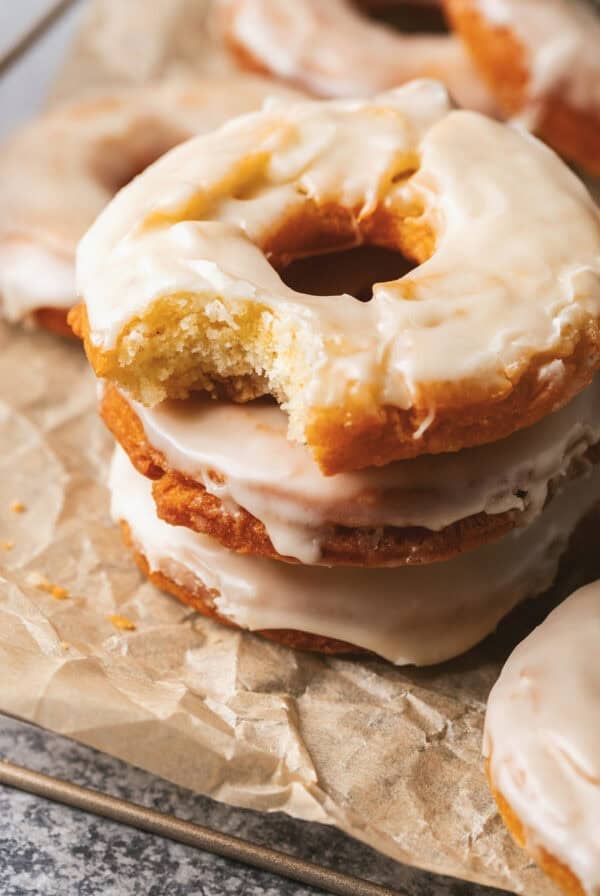 A stack of old fashioned sour cream donuts with the top one missing a bite.