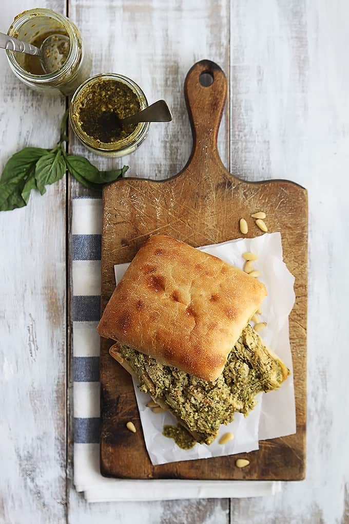 top view of a pesto chicken sandwich on a wooden cutting board with jars of pesto on the side.