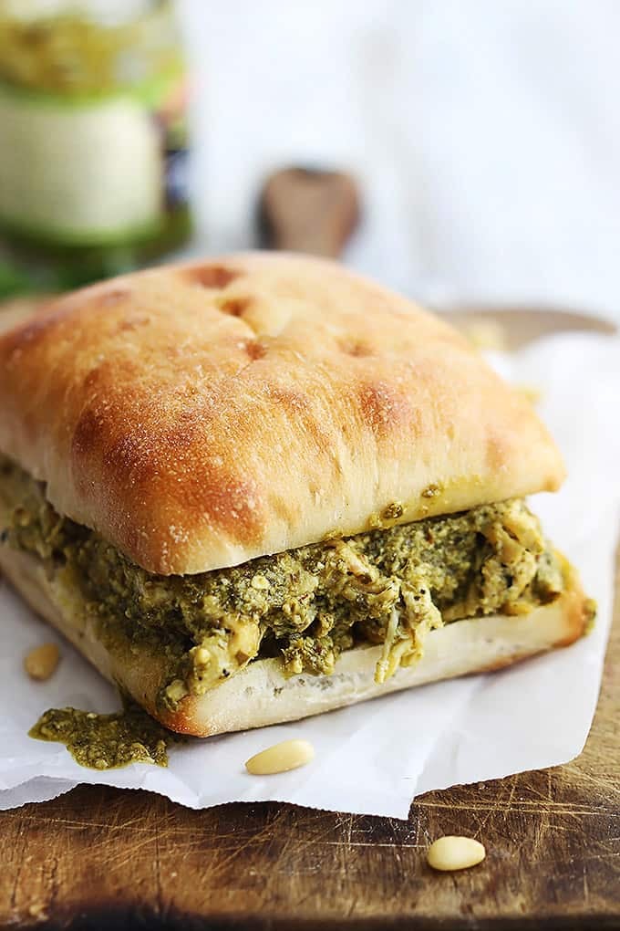 a pesto chicken sandwich on a wooden cutting board.