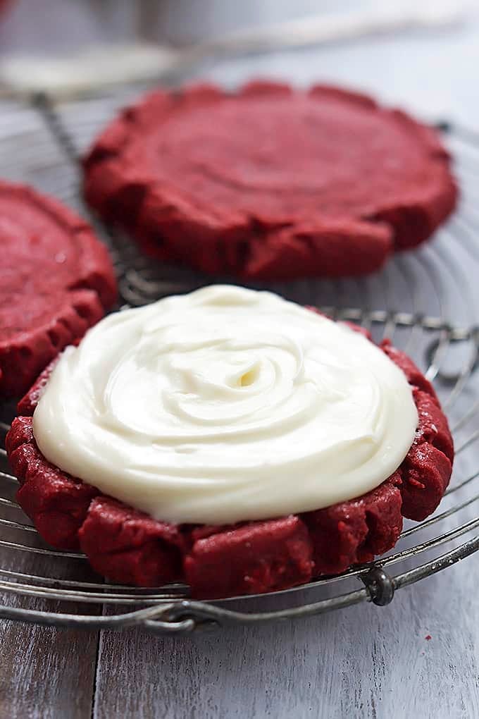 close up red velvet sugar cookies on an iron rack with the front cookie frosted.