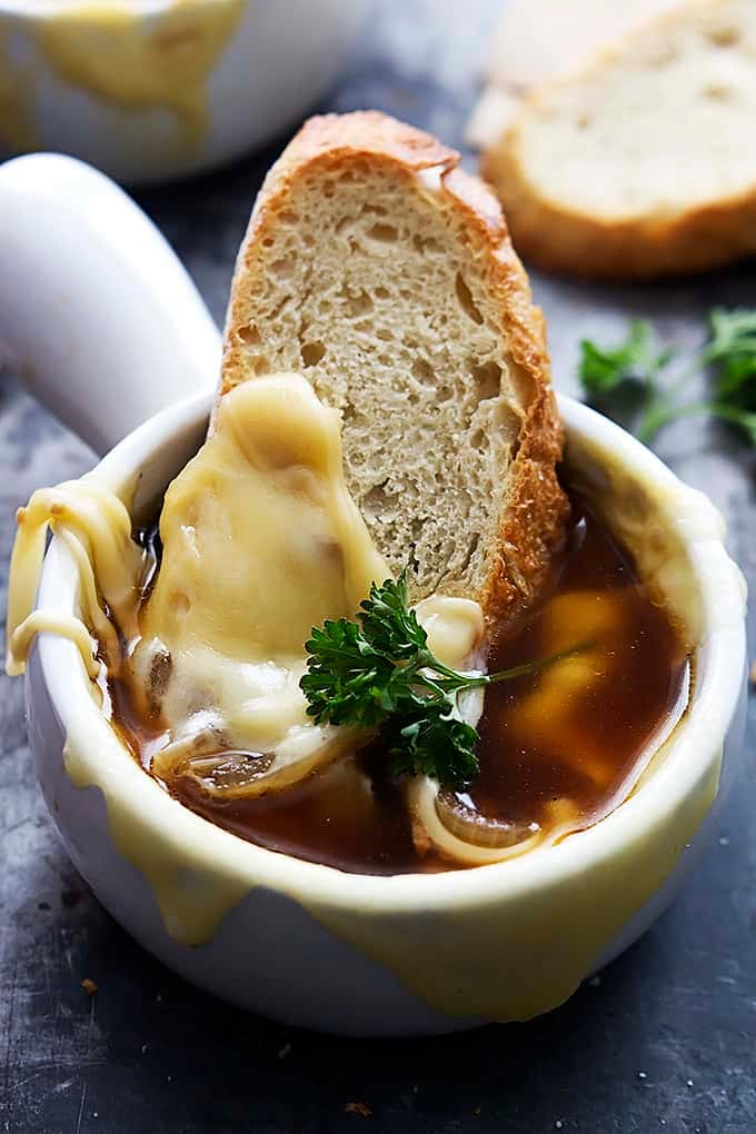French onion soup in a bowl with a slice of bread dipped inside.