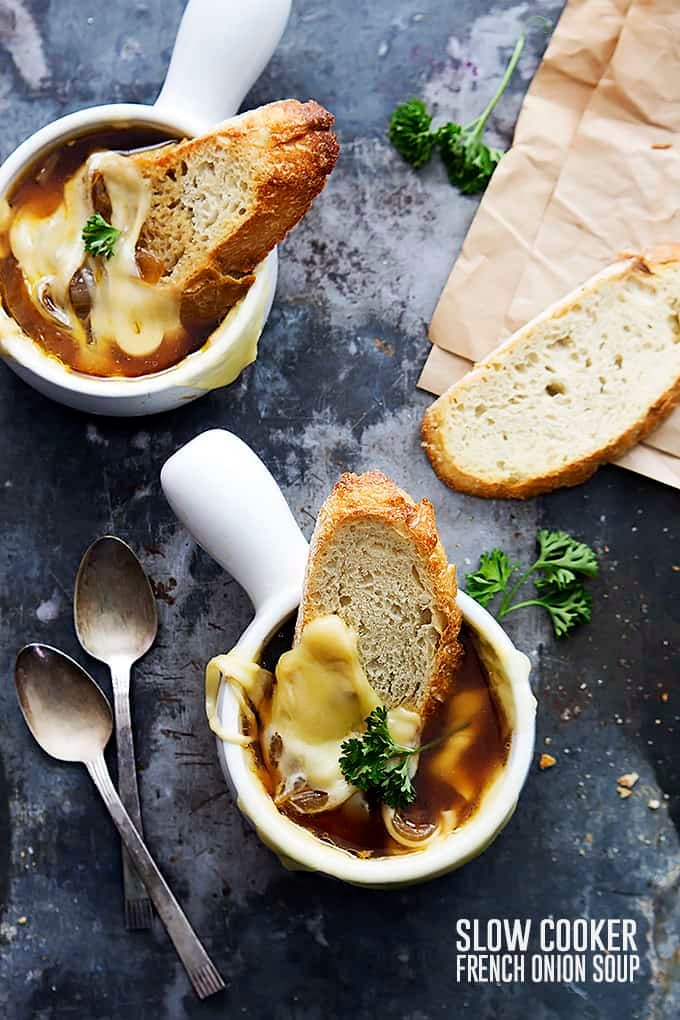 top view of a couple bowls of French onion soup with slices of bread dipped inside and spoons on the side.