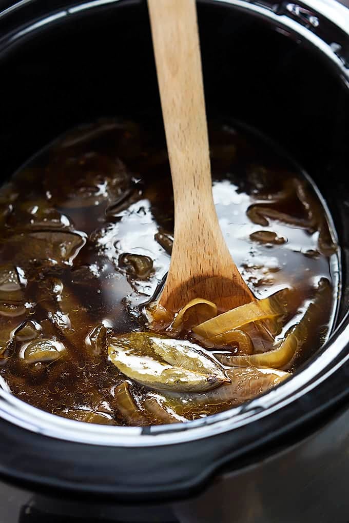 close up top view of French onion soup in a slow cooker with a wooden serving spoon. 