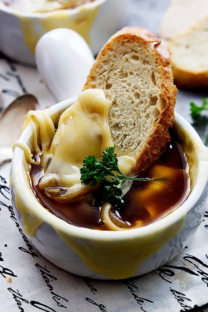 close up of a bowl of French onion soup with a slice of bread dipped inside.