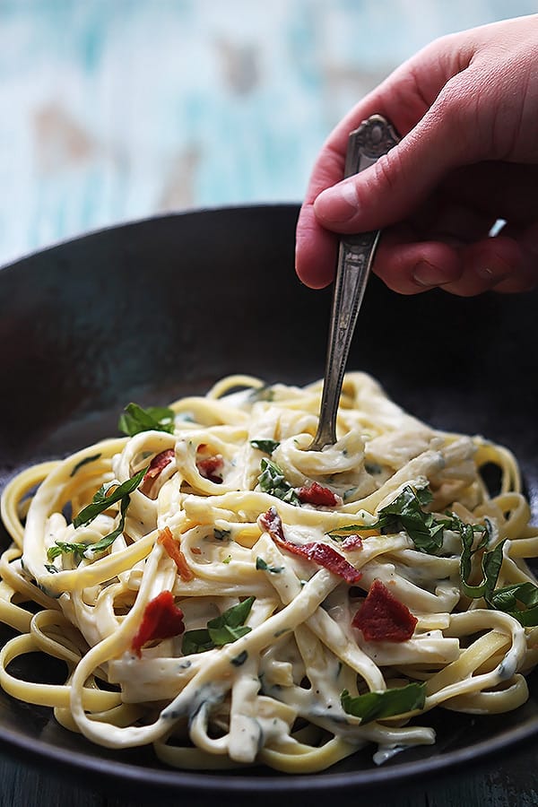 a hand twisting a fork around healthy spinach fettuccine in a bowl.