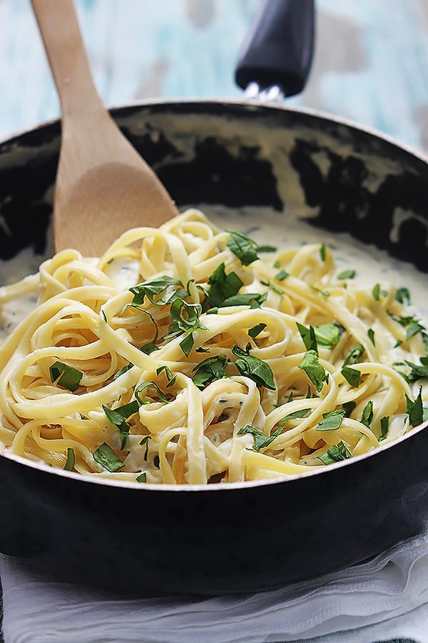 healthy spinach fettuccine in a skillet with a wooden serving spoon.