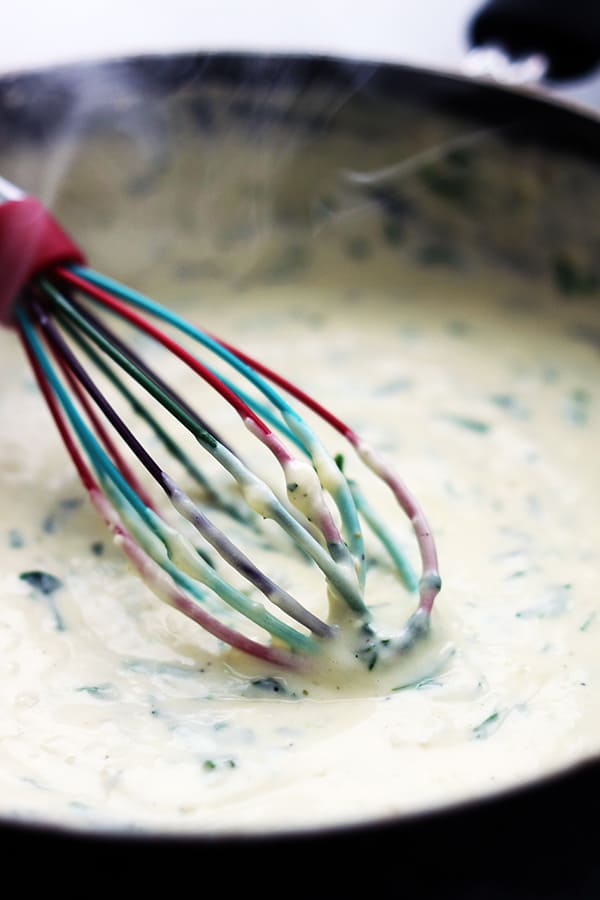 spinach fettuccine sauce in a skillet with a whisk.