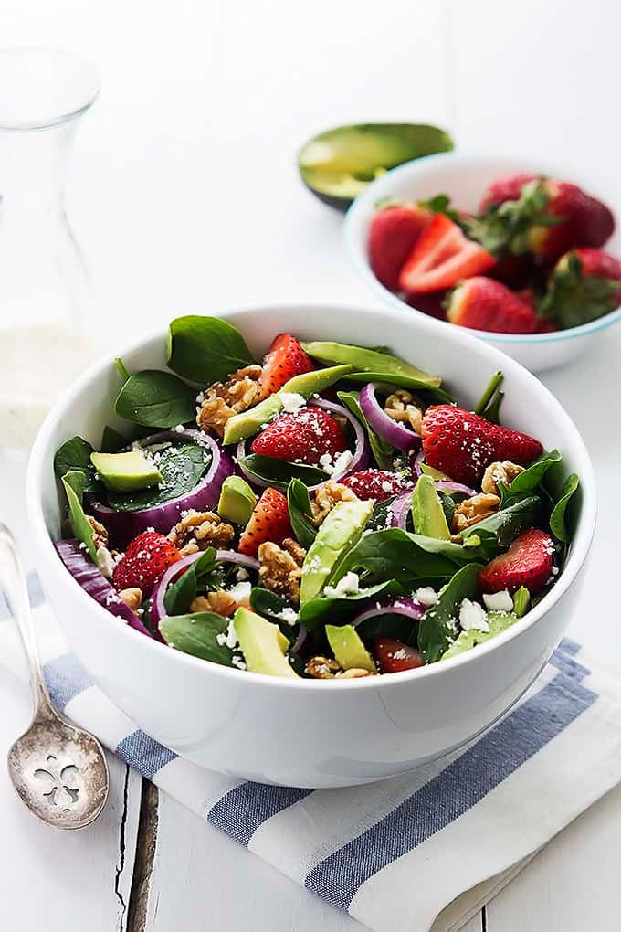 strawberry avocado spinach salad in a bowl with a bowl of strawberries in the background.