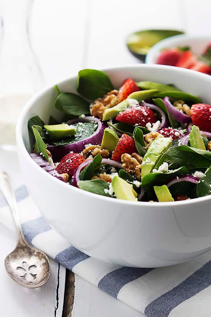 strawberry avocado spinach salad in a bowl with a spoon on the side.