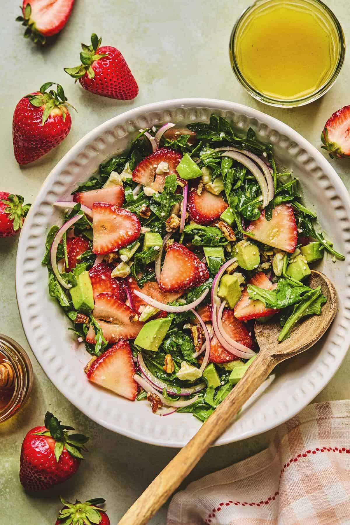 Overhead of strawberry avocado salad and a wooden serving spoon in a serving bowl.
