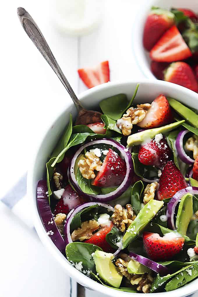 top view of strawberry avocado spinach salad and a fork in a bowl with a bowl of strawberries on the side.