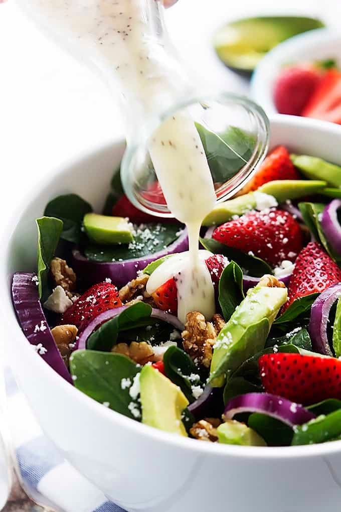 close up of dressing being poured on top of strawberry avocado spinach salad in a bowl.