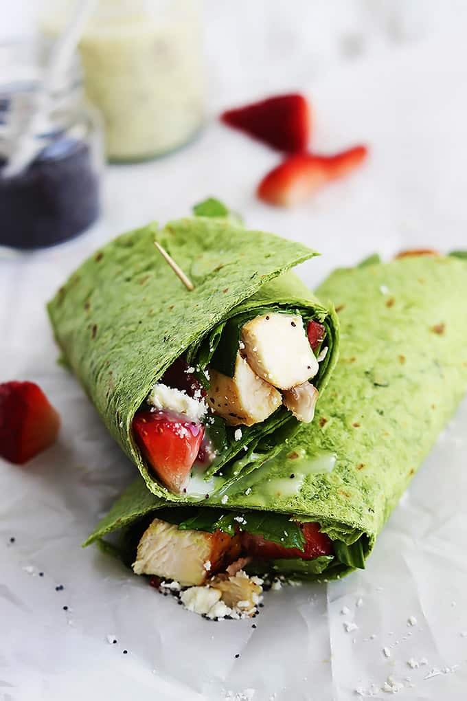 stacked strawberry chicken bacon & spinach wraps with poppyseed dressing with strawberry slices, and jars of dressing and poppyseeds in the background.