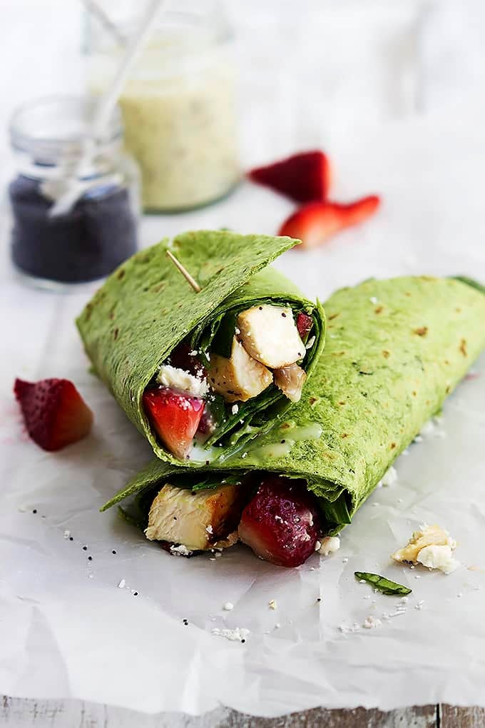 strawberry chicken bacon & spinach wraps with poppyseed dressing stacked on top of each other with a jar of dressing in the background.