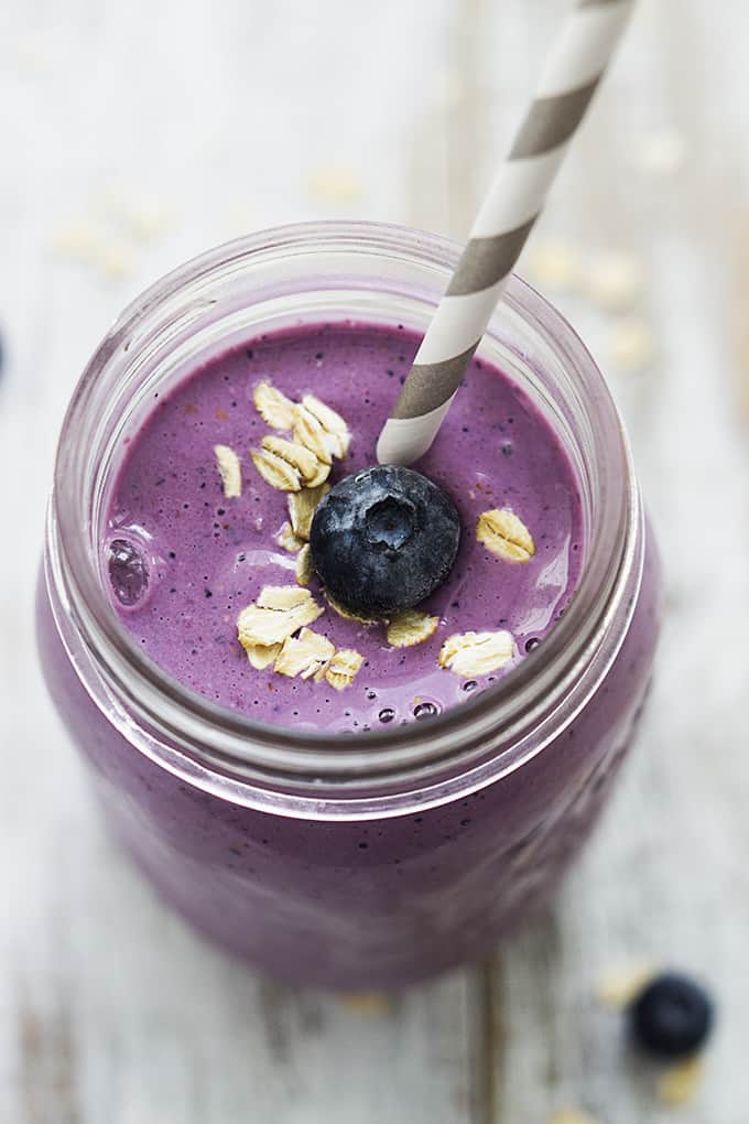 top view of berry oat breakfast smoothie in a jar with a straw and topped with oats and a blueberry.