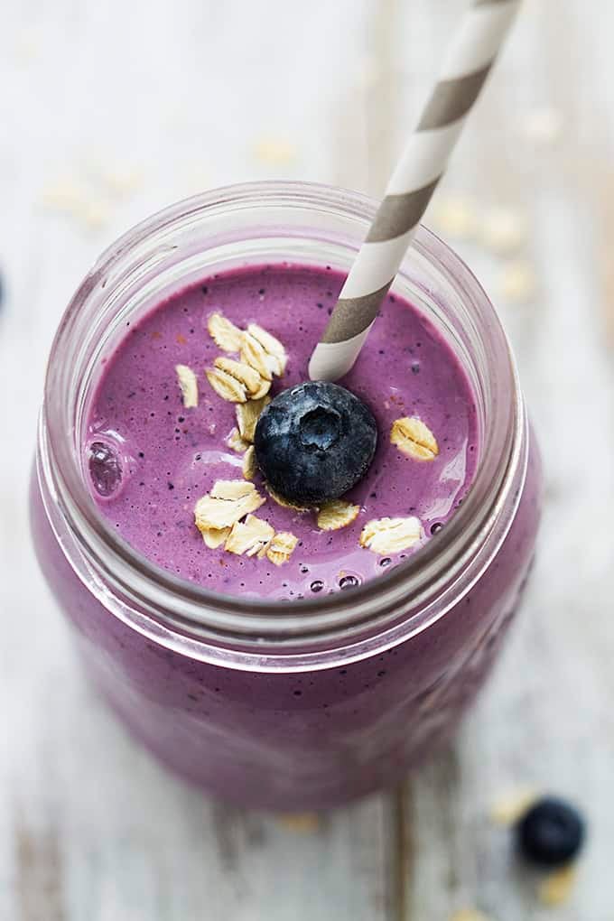 top view of berry oat breakfast smoothie in a jar with a straw and topped with oats and a blueberry.