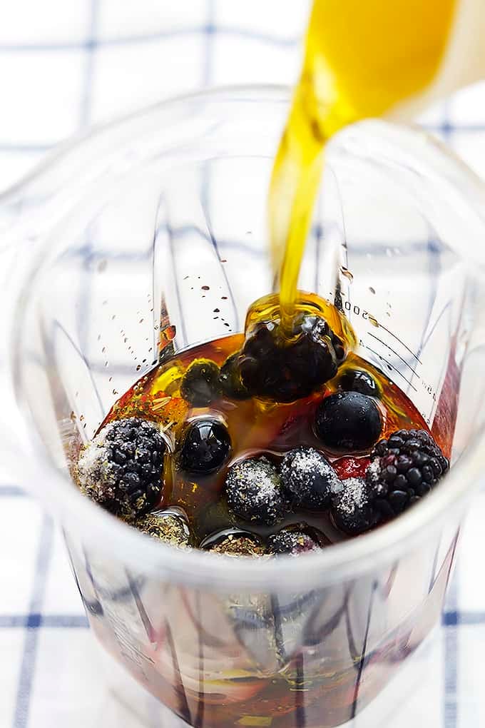 berry vinaigrette ingredients unmixed in a blender with oil being poured inside.