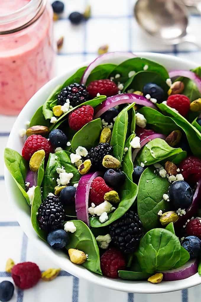berry lover's spinach salad with berry vinaigrette in a bowl next to a jar of vinaigrette.