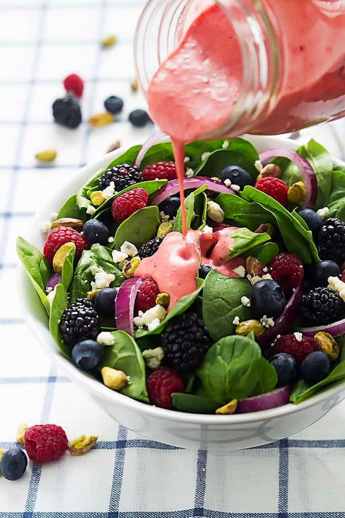 berry lover's spinach salad in a bowl with berry vinaigrette being poured on top from a jar.