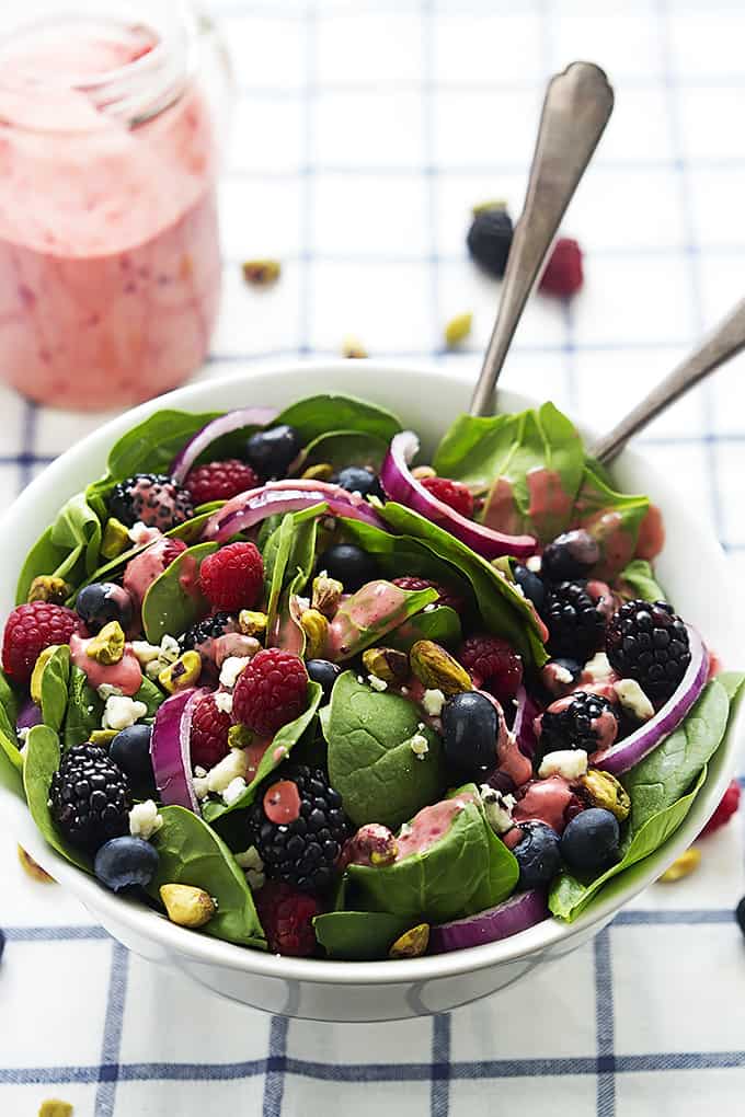 berry lover's spinach salad with berry vinaigrette in a bowl with two spoons next to a jar of vinaigrette.