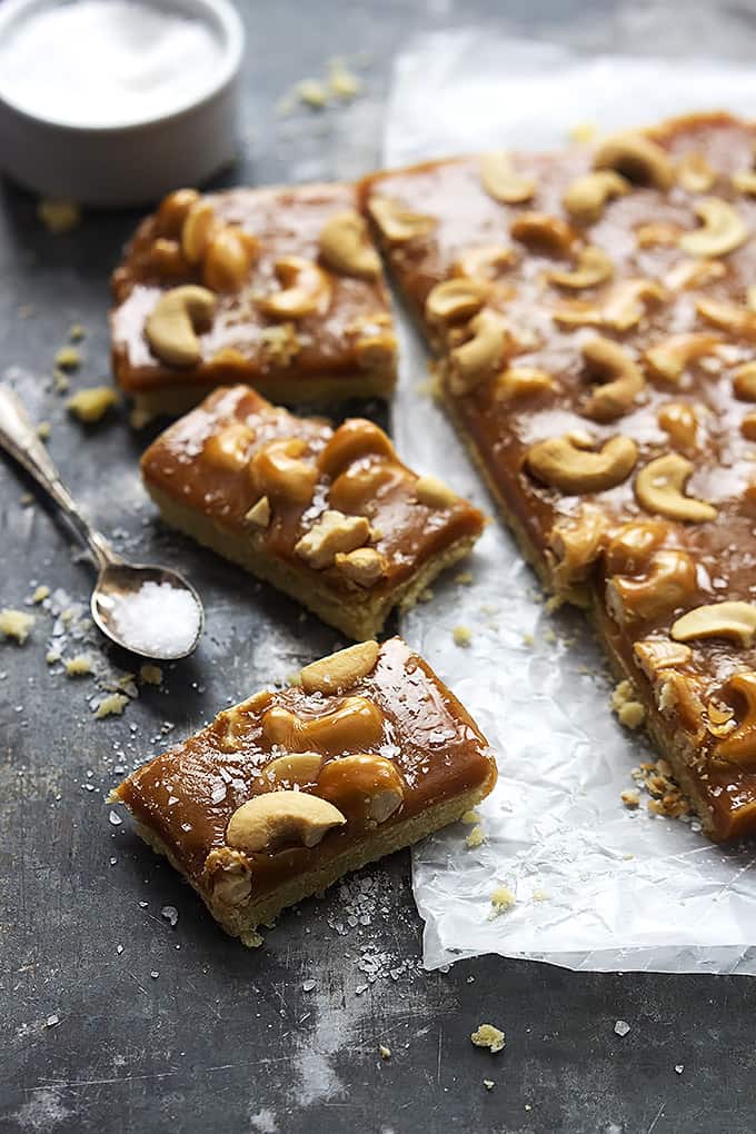 caramel cashew shortbread bars with a spoon and bowl full of salt on the side.