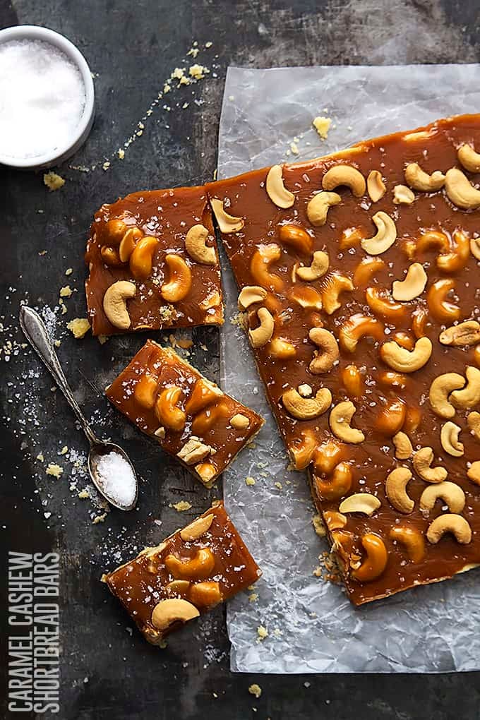 top view of caramel cashew shortbread bars with a spoon and bowl full of salt on the side and the title of the recipe written vertically on the bottom left corner of the image.