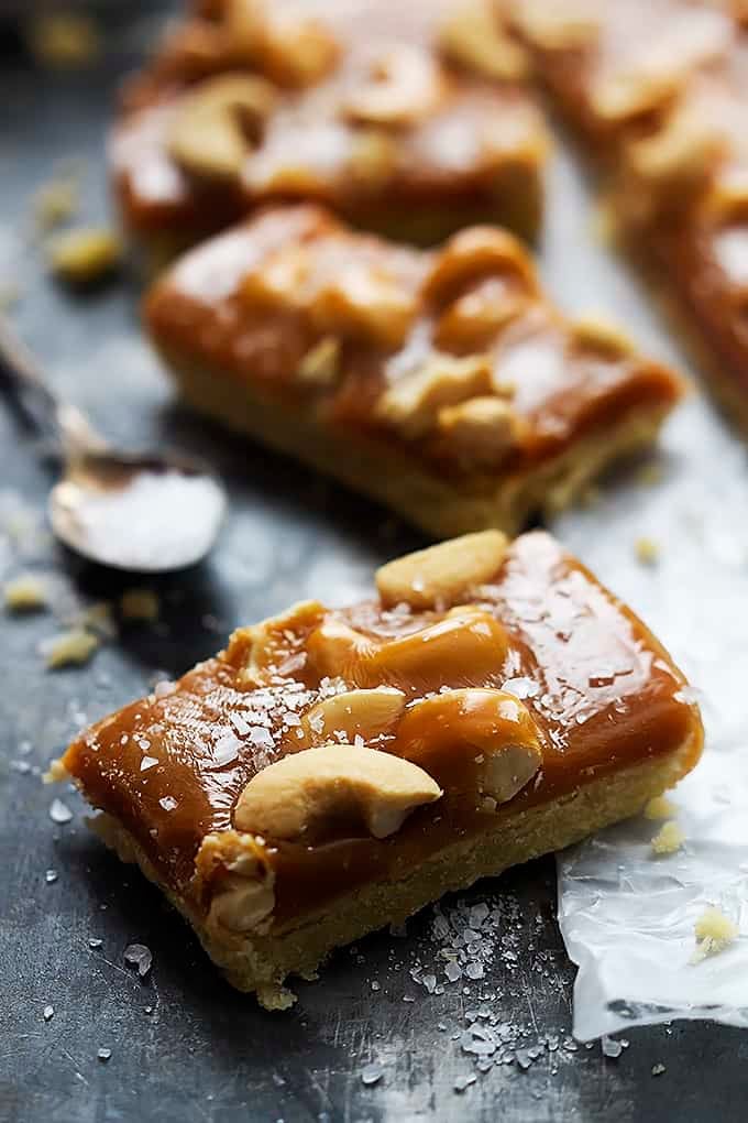 a caramel cashew shortbread bar with a spoon and more bars in the background.