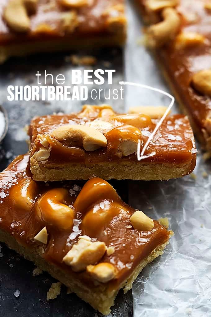 stacked caramel cashew shortbread bars with the words "the best shortbread crust" written on the image with an arrow pointing to the crust on the top bar.