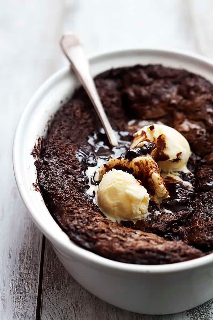 chocolate cobbler topped with vanilla ice cream with a spoon in a serving bowl.