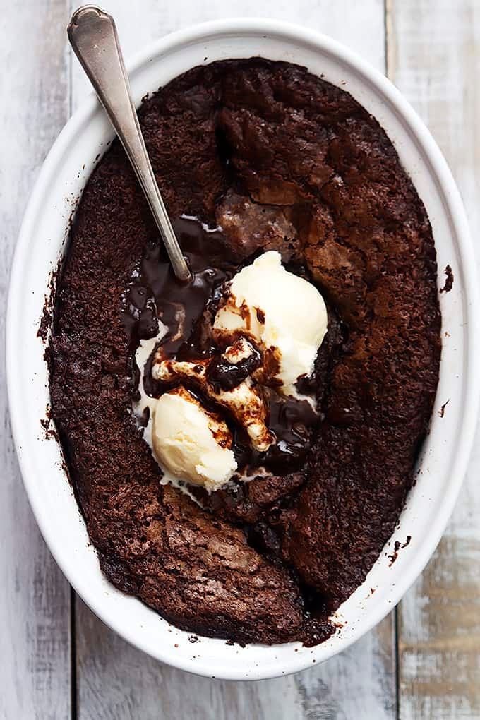 top view of chocolate cobbler with a spoon and vanilla ice cream in a serving bowl.