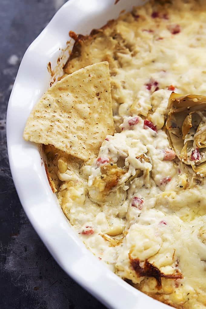 close up top view of feta artichoke dip in a round serving bowl with a chip on top.