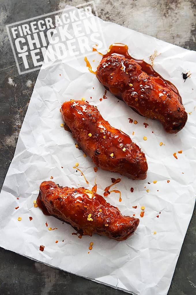 baked firecracker chicken tenders on parchment paper with the title of the recipe written on the top left corner of the image.