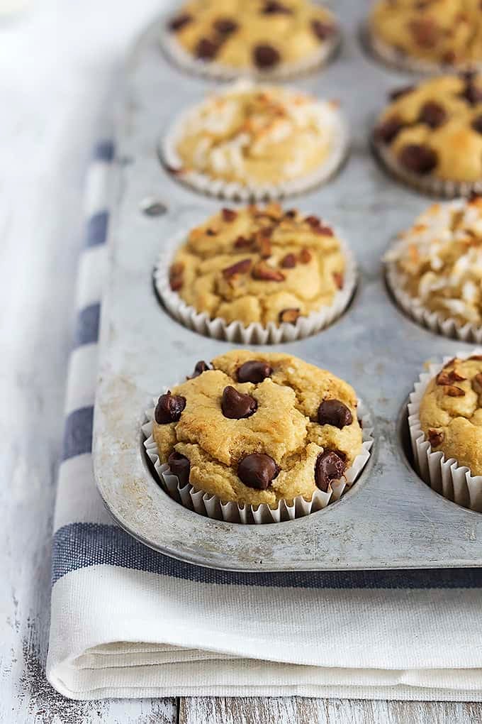 flourless banana blender muffins in a muffin tin with chocolate chips, nuts, or coconut shavings on top.
