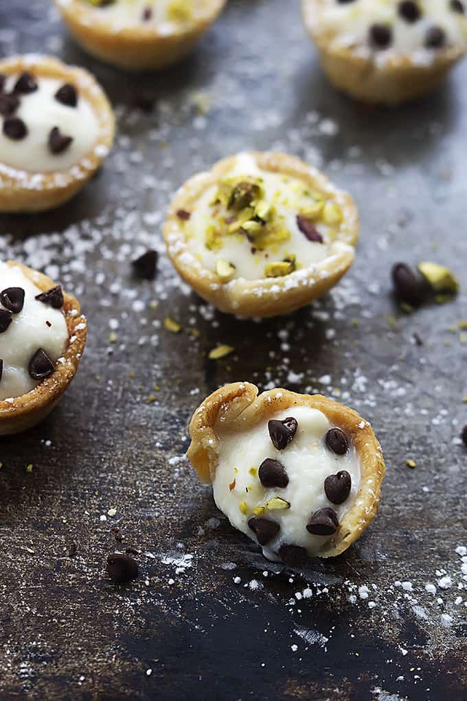 a cannoli bite topped with chocolate chips with a bite missing with more bites in the background topped with chocolate chips or pistachios.