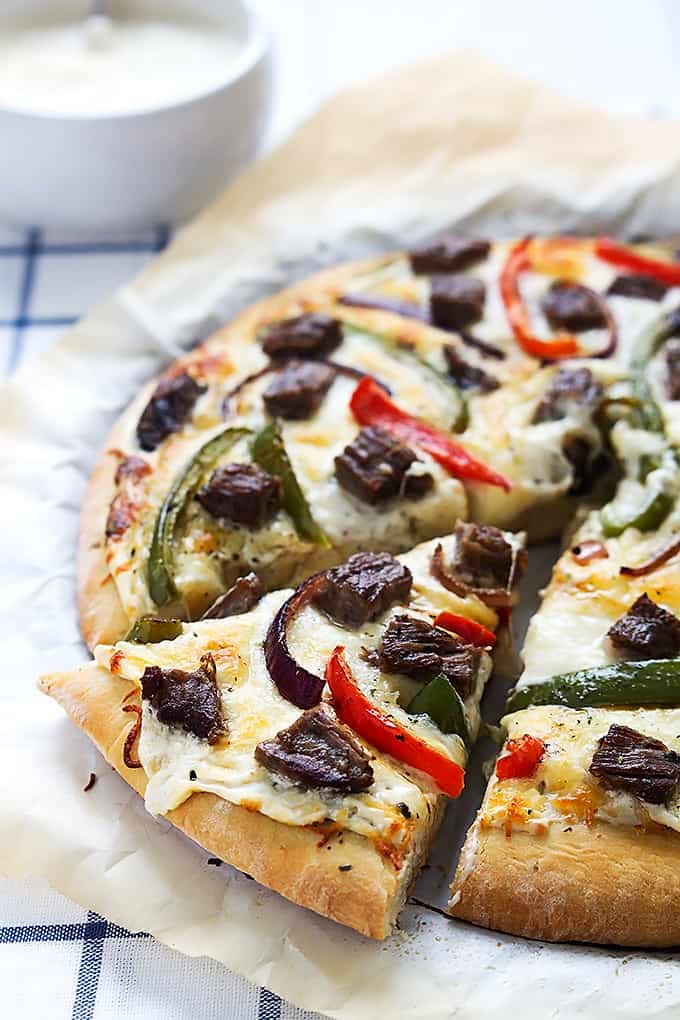 a slice of Philly cheesesteak pizza with the rest of the pizza on the side.