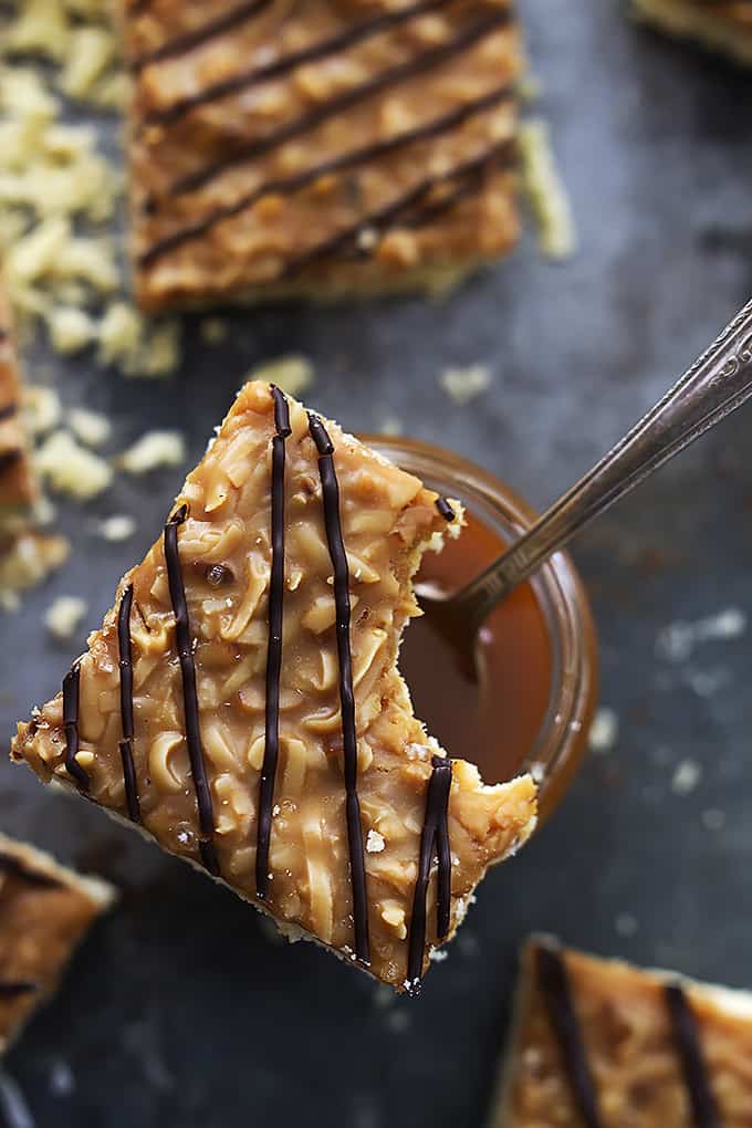 top view of a jar of caramel with a spoon with a Samoa bar with a bite missing sitting on top.