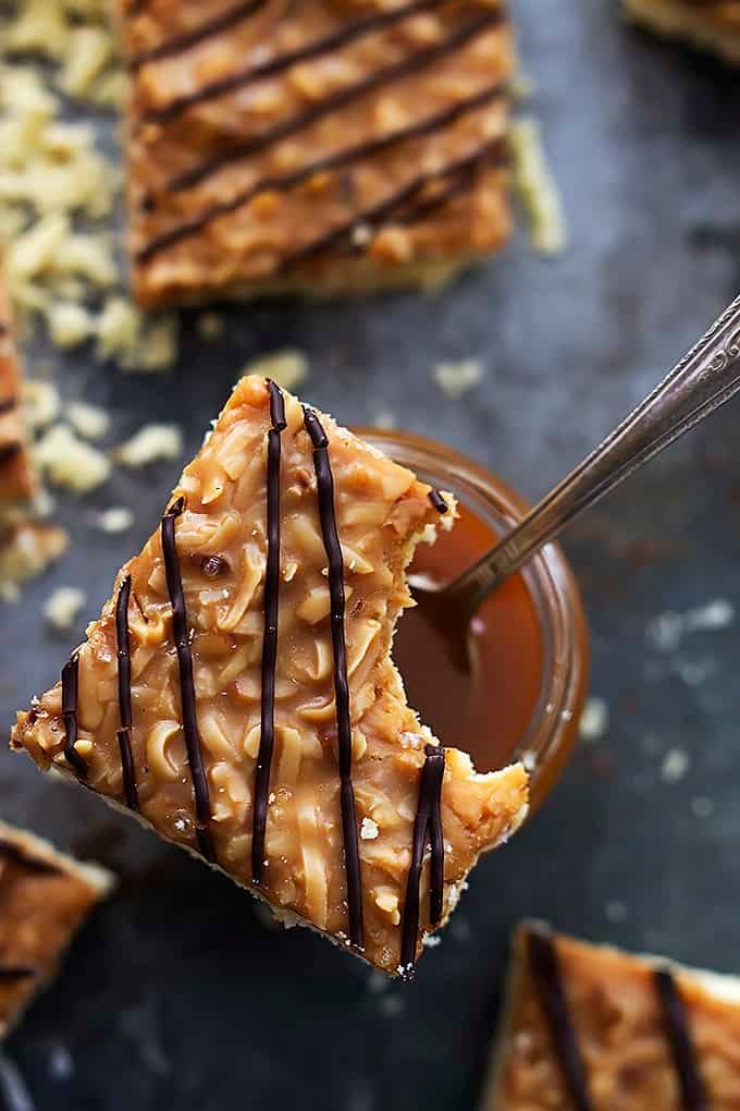 top view of a jar of caramel with a spoon with a Samoa bar with a bite missing sitting on top.