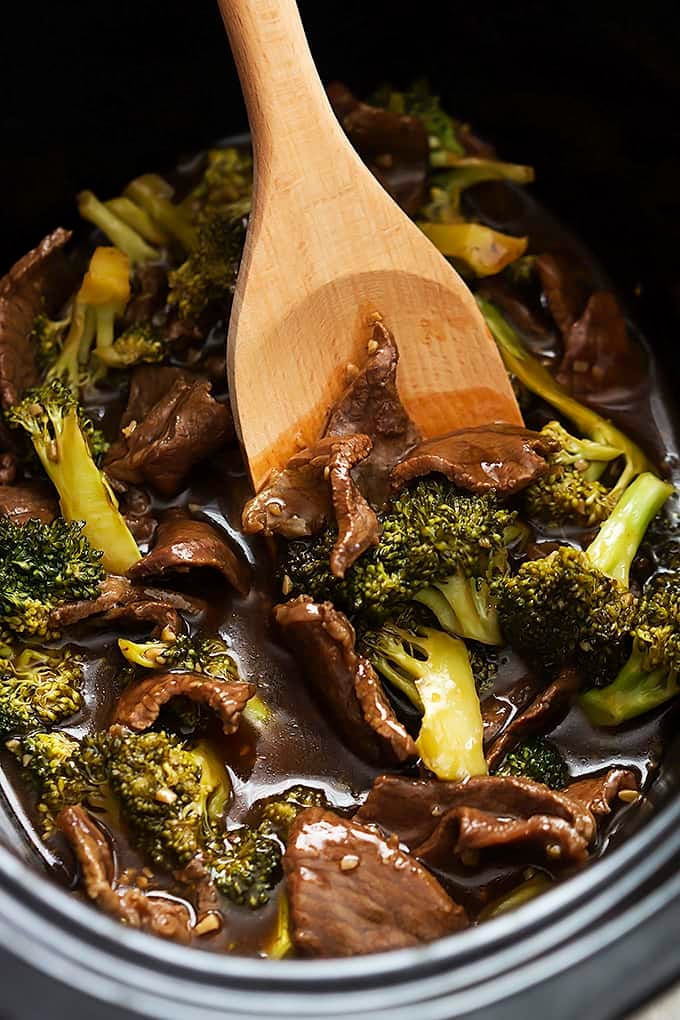 close up of slow cooker broccoli beef and a wooden serving spoon in a slow cooker.
