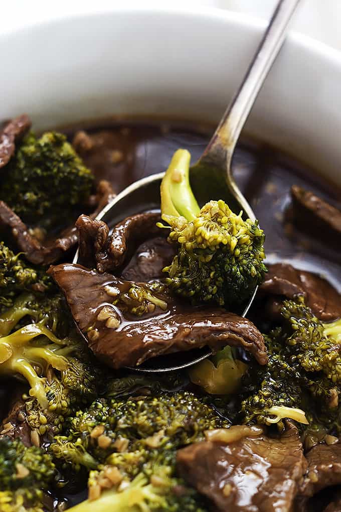 close up of a spoon with a scoop of slow cooker broccoli beef on it in a bowl.